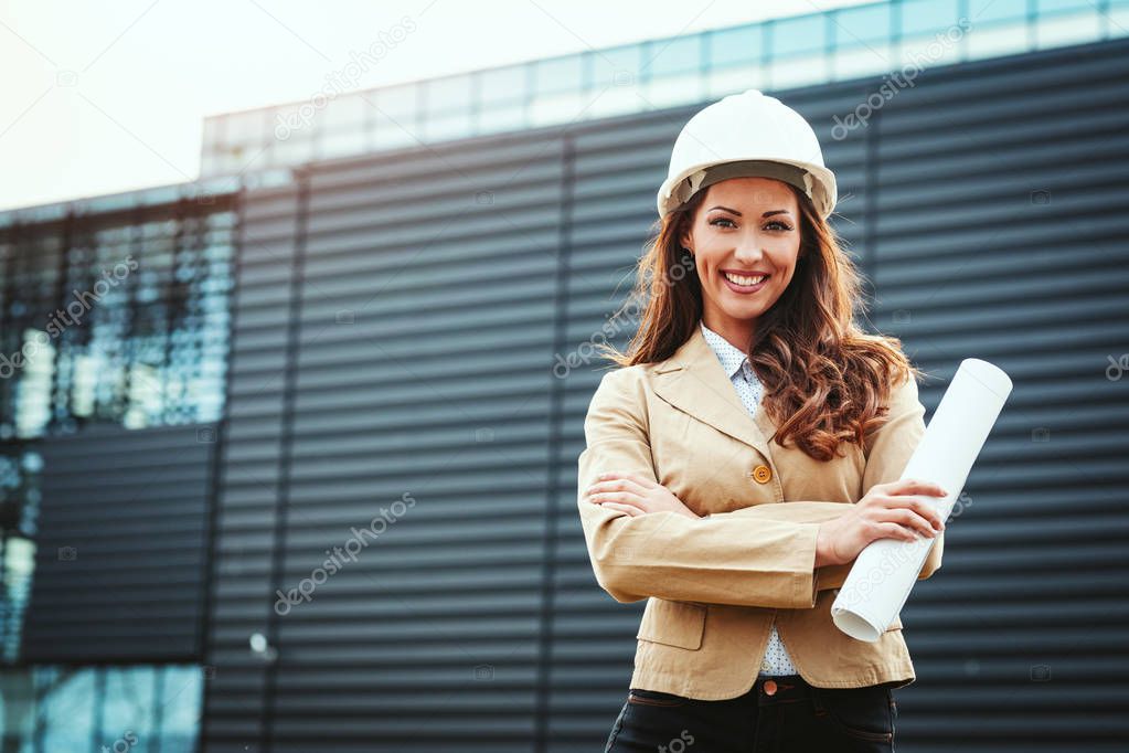 Young successful female engineer holding blueprints at construction site 