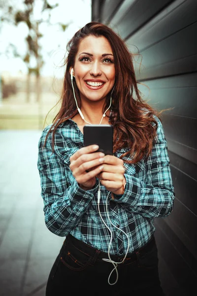 young smiling woman listening to music on smartphone in office district