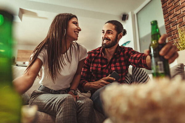 Excited couple playing video games and drinking beer at home on sofa