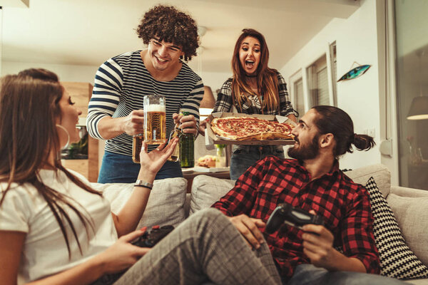 Group of cheerful friends having fun and eating pizza at home