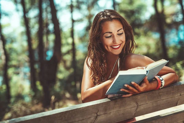 日当たりの良い森のベンチに本を読む若い女性 — ストック写真