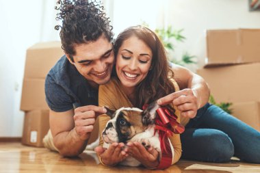 young happy couple lying down on  floor and hugging little puppy in new home