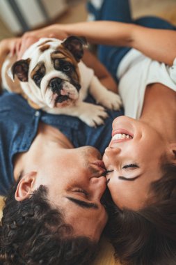 young happy couple lying down on  floor and hugging little puppy in new home