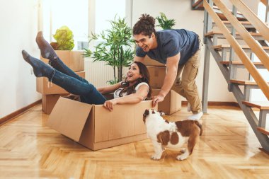 Young couple with little puppy resting after unboxing in new home clipart