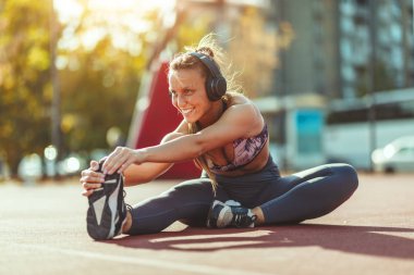 Young fitness woman in headphones doing stretching exercise on public place