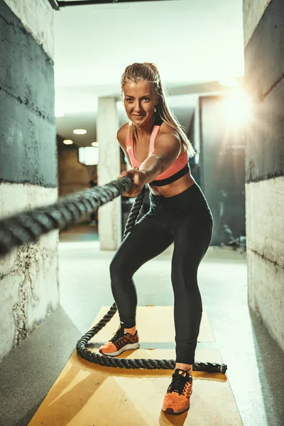 Young muscular woman exercising with rope at gym