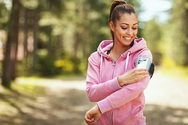 Happy woman checking smartphone in  break of exercises in sunny forest