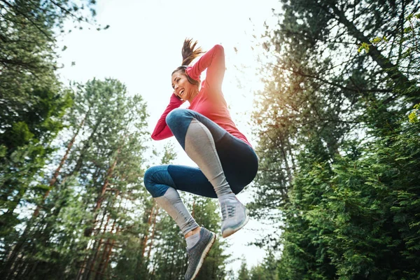 年轻快乐的女跑步者在阳光灿烂的森林里跳跃 — 图库照片