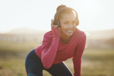 Genç mutlu bayan koşucu, dağlarda gün batımında koşmadan önce müzik dinliyor ve esniyor.