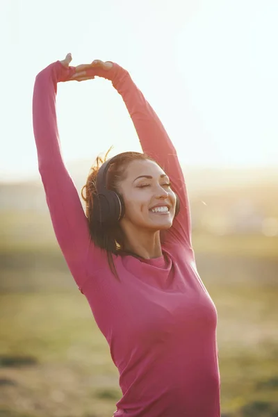 若い幸せな女性のランナーは音楽を聞いて山の中で日没でジョギングする前にストレッチ — ストック写真