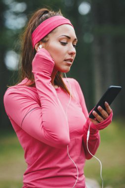 Genç bayan koşucu müzik dinliyor ve güneşli ormanda koşudan sonra mola veriyor.