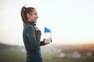 Genç bayan su içiyor ve dağlarda koşuya hazırlanıyor.