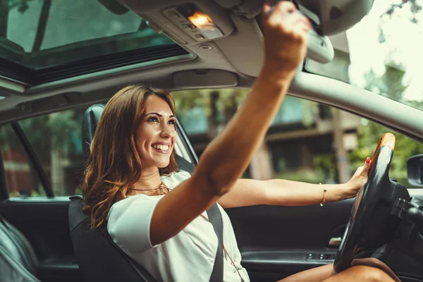 Hermosa Joven Mirando Través Del Espejo Retrovisor Mientras Conduce Coche — Foto de Stock