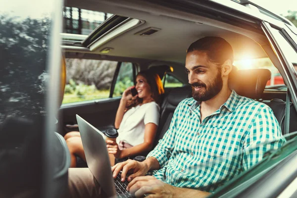 Young confident business partners working on business trip on back seat in car