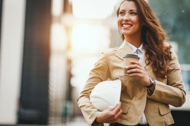 Genç kadın mimar kahve içme ve kentsel şehir arka planda elinde kask tutarak