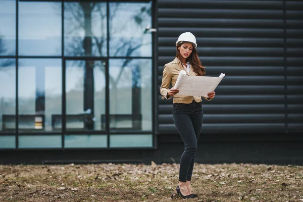 Portrait of young engineer woman in white helmet holding blueprints at construction site