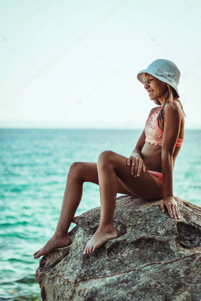 Happy teenager girl relaxing on rocky beach at sunset