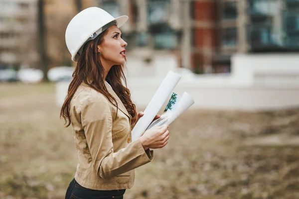 Portrait of young engineer woman in white helmet holding blueprints at construction site
