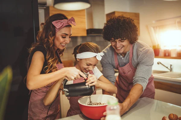 Young parents with daughter preparing dough for muffins in kitchen