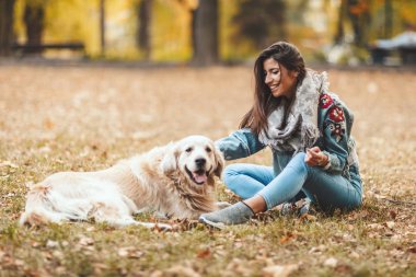 yapraklarla kaplı ve köpek ile eğleniyor zeminde oturan genç kadın