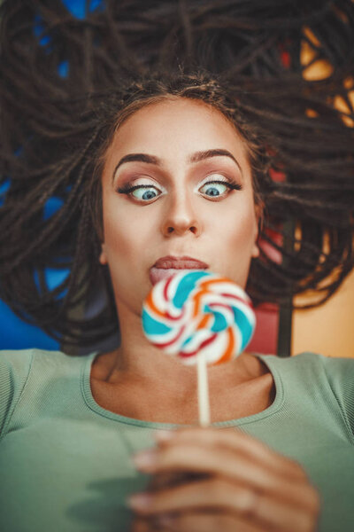 Cheerful young woman with long afro braided hair licking lollipop