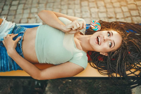 ロリポップを保持する長いアフロ編組ヘアを持つ陽気な若い女性 — ストック写真