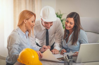 Üç profesyonel mimardan oluşan bir ekip, ofisteki mimari planları inceliyor..