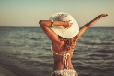 Beyaz bikinili güzel bir kadın kafasında beyaz şapkayla gün batımının tadını çıkarıyor.. 