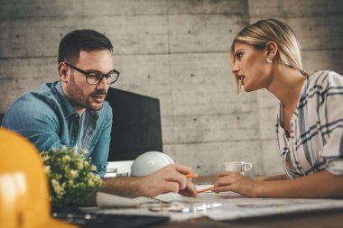 Yeni bir proje üzerinde çalışan iki genç mimar ofis planlarını analiz ediyor.