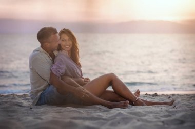 Çift birbirine bakıyor ve kumsalda gülümsüyor.