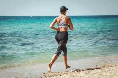 Orta yaşlı, kaslı bir kadın, deniz sahilinde sıkı antrenman yapıyor.