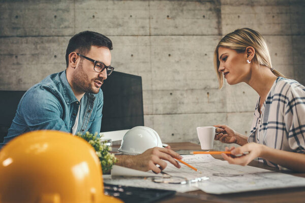 Two young architect colleagues working on new project, analyzing blueprints in office