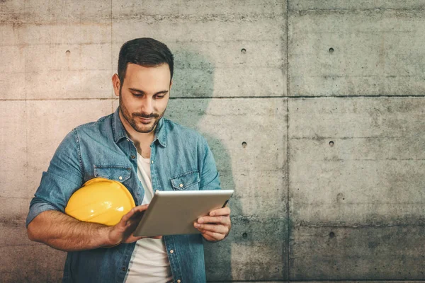 Young handsome entrepreneur looking on digital tablet, checking plans before starting work on construction site