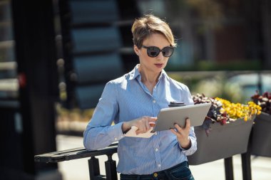 Olgun iş kadını tatilde ofis önünde dijital tablet kullanıyor.