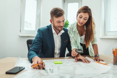 İki başarılı genç mimar yeni bir proje üzerinde çalışıyor ve ofis planlarını analiz ederken iletişim kuruyorlar..