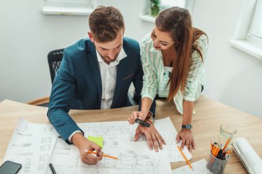 İki başarılı genç mimar yeni bir proje üzerinde çalışıyor ve ofis planlarını analiz ederken iletişim kuruyorlar..