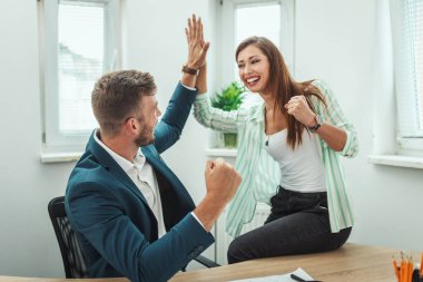 Genç ve başarılı iş adamları, gündelik ofiste yeni bir proje üzerinde çalışırken başarıyı kutluyorlar..