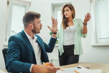 İki genç endişeli mimar, ofisteki yeni bir projenin planlarında bulunan sorunları analiz ediyor..