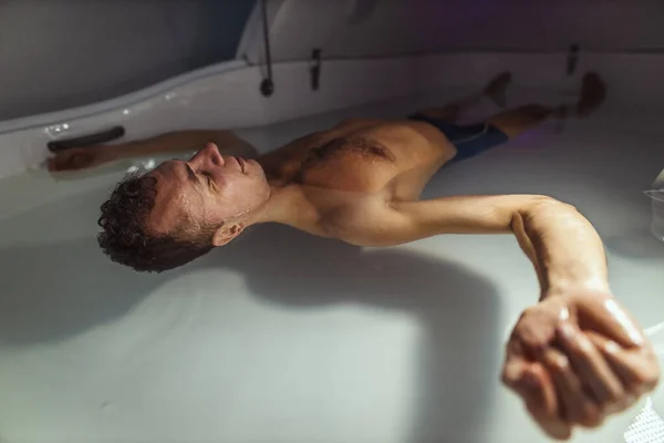 Relaxed man is floating in a sensory deprivation tank. He is very relaxed. Welness and Spa concept.