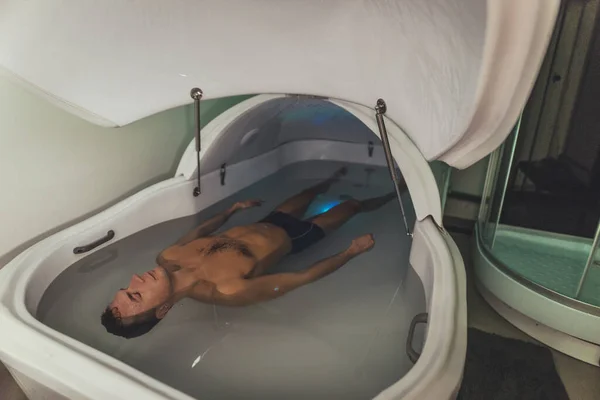 Relaxed man is floating in a sensory deprivation tank. He is very relaxed. Welness and Spa concept.