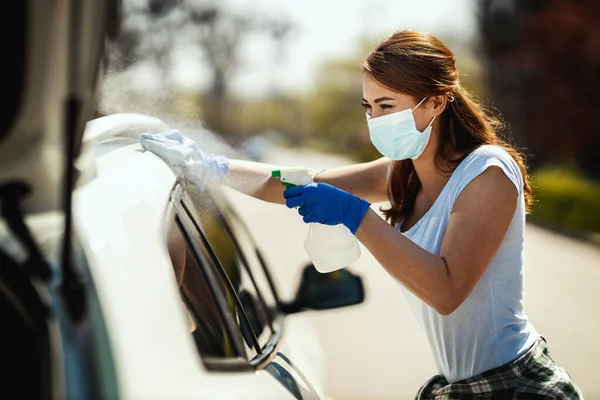 顔にマスクをし 手に手袋をしている若い女性は 片方の布を持っている彼女の車ともう一方の手で消毒薬とボトルを拭く — ストック写真