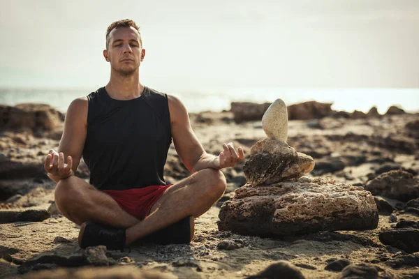 A handsome man is doing yoga at the sea beach in summer sunny day.