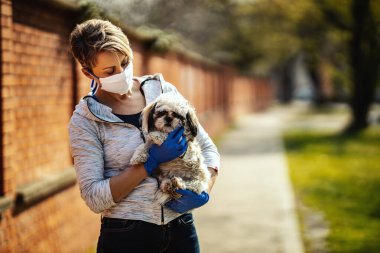 Tıbbi koruyucu maskeli bir kadın, grip salgını ve koronavirüs salgını sırasında şehrin sokaklarında sevgili küçük Shih Tzu köpeğiyle vakit geçiriyor..