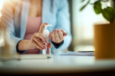 Tanınmayan bir iş kadınının yakın çekimi, grip virüsü salgını ve koronavirüs salgını sırasında enfeksiyonu önlemek için iş yerinde el dezenfeksiyonu için antibakteriyel jel kullanır..