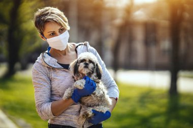 Tıbbi koruyucu maskeli bir kadın, grip salgını ve koronavirüs salgını sırasında şehrin sokaklarında sevgili küçük Shih Tzu köpeğiyle vakit geçiriyor..