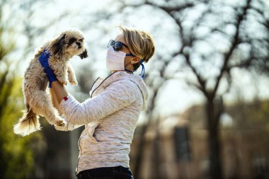 Tıbbi koruyucu maskeli bir kadın, grip salgını ve koronavirüs salgını sırasında şehrin sokaklarında sevgili küçük Shih Tzu köpeğiyle vakit geçiriyor..