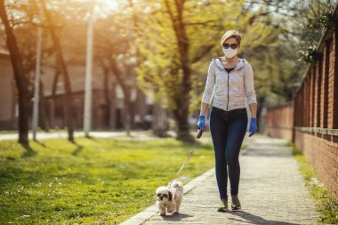 Tıbbi koruyucu maskeli bir kadın, alerji ya da grip virüsü salgını ve koronavirüs salgını sırasında sevgili küçük Shih Tzu köpeğiyle şehir yolunda yürüyor..
