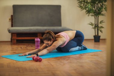 Genç, gülümseyen bir kadın oturma odasında esneme egzersizleri yapıyor. Sabah güneşinde paspasın üzerinde..