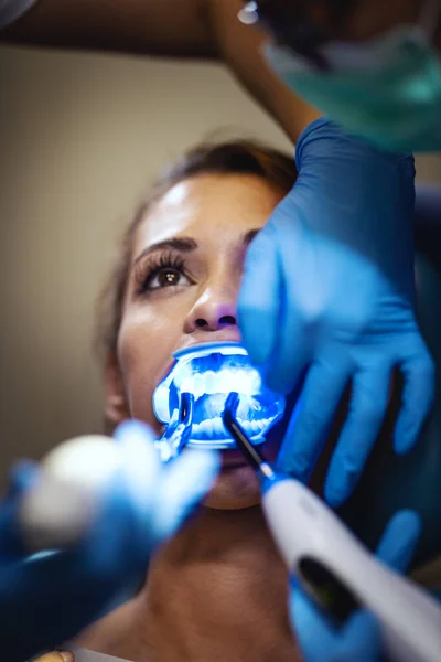 その美しい若い女性は歯医者にいる 歯医者の椅子に座り歯の上に歯のブレースをつけ赤外線ランプで美学的な自己整合言語ロックをかける — ストック写真