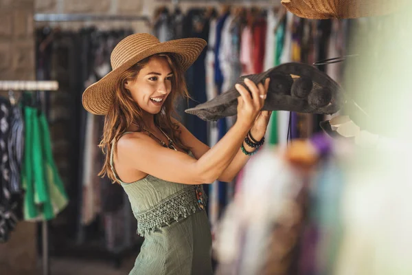 一位美丽的微笑的年轻女子正沿着地中海小镇的街道散步 在夏日阳光明媚的日子里尽情享受着 她选了一顶新帽子 想买它 — 图库照片